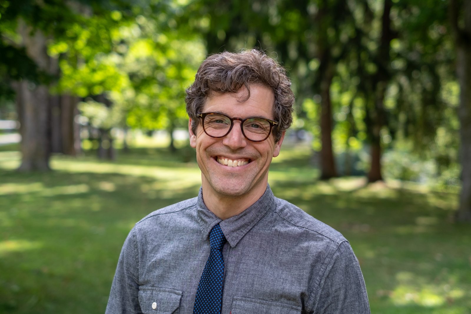 Dan Atkinson, smiling, outdoors among trees.