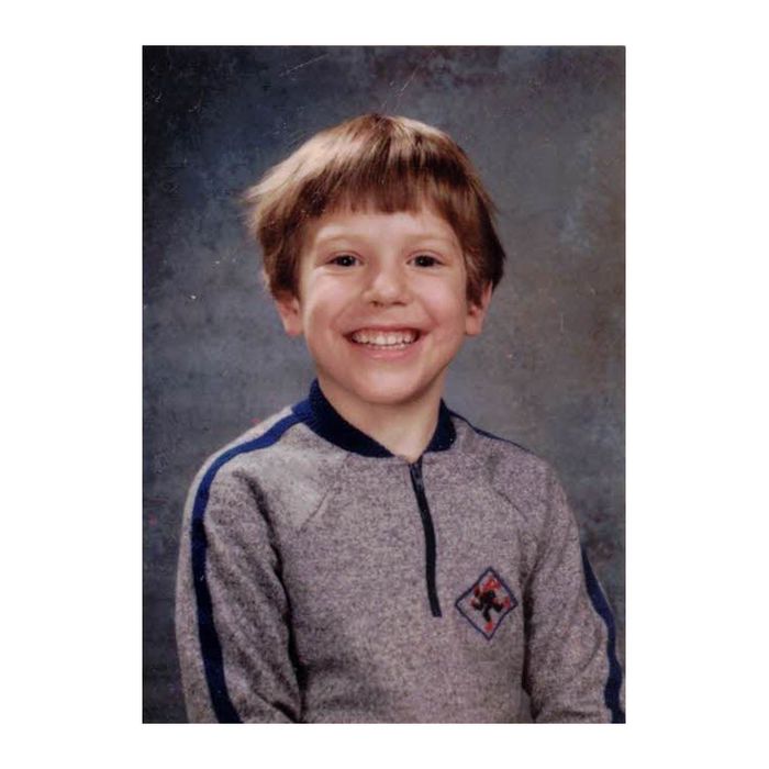 Dan Atkinson as a young boy in a school portrait, grinning, in a grey zip-neck sweater with a small crest on the chest.