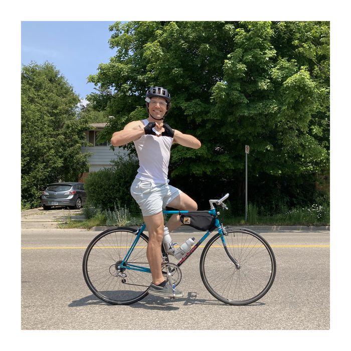 Dan Atkinson astride his teal road bike in a helmet and cycling gloves, making a heart shape with his hands.